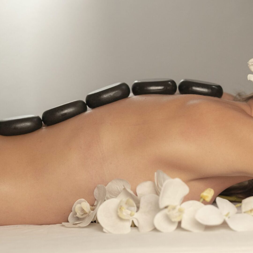A woman laying down with many black stones on her body.